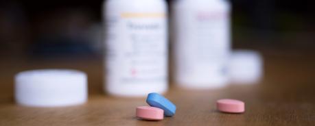 Vor zwei geöffneten Tablettendosen liegen zwei rosane und eine blaue Tablette.